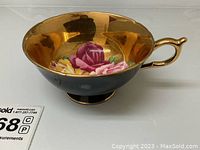 Side view of the cup showing black exterior and reflective gold interior with floral design