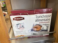 Box with image and branding of the Bravetti professional food slicer showing product usage and features in French (Trancheuse alimentaire professionnelle).