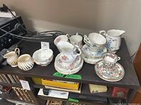 Photo showing assortment of china on a table including cups, saucers, cream and sugar containers, stacked plates