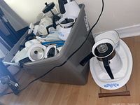 Grey plastic bin filled with white enameled CorningWare items in blue cornflower pattern.