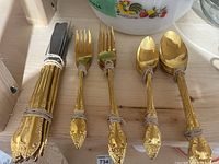 Full layout of gold flatware grouped by type on wooden shelf