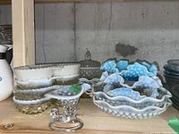 Group of white milk glass hobnail bowls, clear jar, blue bowls and footed dish on wooden shelf