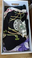 Top-down view of white storage box containing stacked folded kimonos: black embroidered, cream printed, purple printed