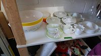Shelf view of various Pyrex bowls, lidded dishes, cup/saucer, milk glass juicers, hobnail creamer and sugar