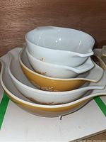 Stacked vintage Pyrex mixing bowls showing yellow floral daisy pattern and pouring spouts with handles.