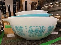 Two stacked white bowls showing turquoise Butterprint motif on white glass exterior.