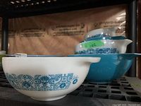 Front white patterned bowl with handle and spout, stack of bowls behind