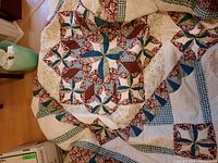 Overall view of the laid out quilt showing star and pinwheel patchwork pattern with maroon, teal blue, cream, and green fabrics.
