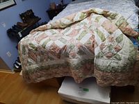 Photo showing the quilt spread over a bed, displaying the overall pattern and color scheme combining pink, green, and white patchwork squares.