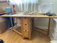Front view of table showing drop-leaf ends, tabletop items (teacups, cover, lantern, carrier, phone)