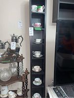 Full view of tall black shelf displaying five teacups with saucers and four additional teacups.