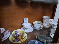 Shelf display of various hand painted teacups and saucers with floral and fruit motifs