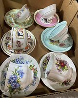 Box containing six different Paragon vintage floral teacups and matching saucers with varying colors and floral designs.