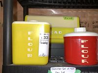 Photo showing two canisters, one yellow and one red, both labeled FLOUR, and a yellow breadbox behind them.