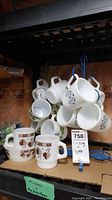 Set of vintage milk glass coffee cups hanging and stacked, showing various patterns and handles, displayed on shelf with lot tag.