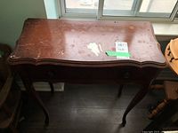 Front view of antique wooden side table showing curved top with visible finish wear and drawer with two round metal pulls.