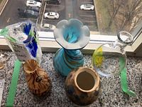Five assorted art glass items on a marble windowsill, showing different glass vases and bottles with varied colors and shapes.