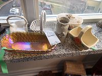 Overview of six baskets and pitcher on window ledge including glass dish and ceramic pieces