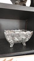 Side angle view of clear glass footed bowl showing pinwheel and starburst cut pattern with scalloped rim and three glass feet.
