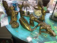 Six brass figurines on a turquoise surface near a window, including figures of a girl with a dog, a boy, an alligator, a cat, a bird, and a sailboat.
