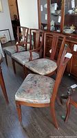 Six wooden dining chairs with floral upholstery arranged in a row, showing overall condition and design.