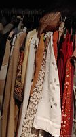 Various women's blouses, sweaters, and jackets hanging on rack, colors include browns, creams, white, orange, with different textures and patterns