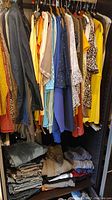 Closet with hanging denim jackets, blouses in various patterns and colors, and folded jeans on shelf below