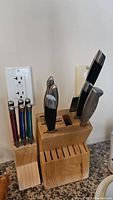 Photo of wooden knife block with metal kitchen knives and utensils including Henckels and Kitchen Aid brands