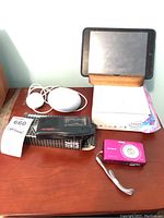 Image showing overall lot contents: Sony Cyber-shot camera, Google Home Mini, Olympus recorder, Apple tablet on stand, Acer Intel box