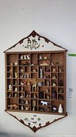 Full front view of wooden wall shelf filled with various ceramic and plastic figurines, showing layout and decorative painting on top and bottom of shelf.