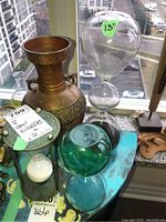 Photo showing a large decorative hammered metal vase, a large clear glass hourglass approx 13 inches tall, and several smaller hourglasses including a turquoise tinted glass globe hourglass.