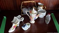 Overview image showing the porcelain shoes, floral teapot, creamer, six small glasses in metal bamboo-handle carrier, and two small decorative bottles.