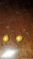 Pair of drop earrings featuring golden-yellow freshwater pearls on 14K gold hooks placed on a dark wooden surface.