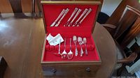 Complete set of silver plated flatware inside the wooden box with red felt lining, including knives, forks and spoons.