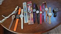 13 assorted wristwatches on a wooden table showing different styles, bands and colors