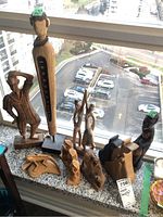 Photo showing nine wood carvings together on a ledge by a window, including standing human figures and smaller carvings.