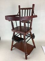 Front angle of antique wooden high chair showing tray, seat, footrest, legs, and spindles.