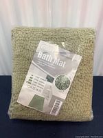 Packaged large green bath mat, showing its compressed state in plastic packaging
