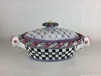 Front view of the closed casserole dish showing chicken heads on the sides, checkered pattern on base and floral lid.