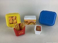 Group photo of all collectible vintage Fisher Price McDonald's food toys showing Chicken McNuggets box, French fries container, BBQ sauce container, waffles box, and blue square container.