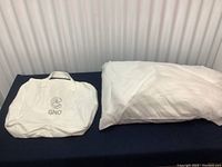 The weighted blanket folded on the right side of the black surface with the white storage bag with GNO logo beside it.