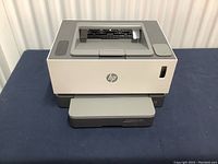 Front angle view of HP LaserJet 1018 printer on a table, showing paper output tray extended and top paper feed opening