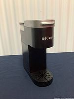 Front view of the black and silver Keurig coffee maker showing the drip tray and front design with logo.