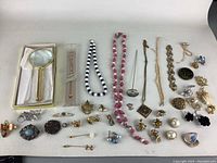 Photo showing entire lot of jewelry with necklaces, brooches, pins, earrings, and a magnifying glass organized on a flat surface