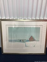 Full view of framed artwork showing winter scene with two figures, fencing, and a house under glass reflecting surroundings.