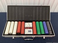 Open aluminum poker case showing rows of poker chips in multiple colors, two decks of cards and red dice inside.