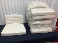 Seven sets of white vinyl cushions stacked with one set displayed showing seat and back cushions together.