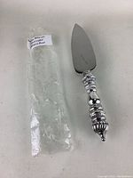 Sterling silver pie/cake lifter with ornate handle and protective bag on a white background.