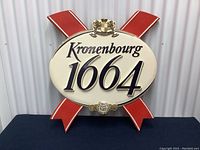 Vintage Kronenburg 1664 beer sign with visible wear, showing front view on a black surface with a corrugated metal background.