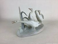 Matte finish porcelain figurine showing three geese and reeds on a sculpted base.